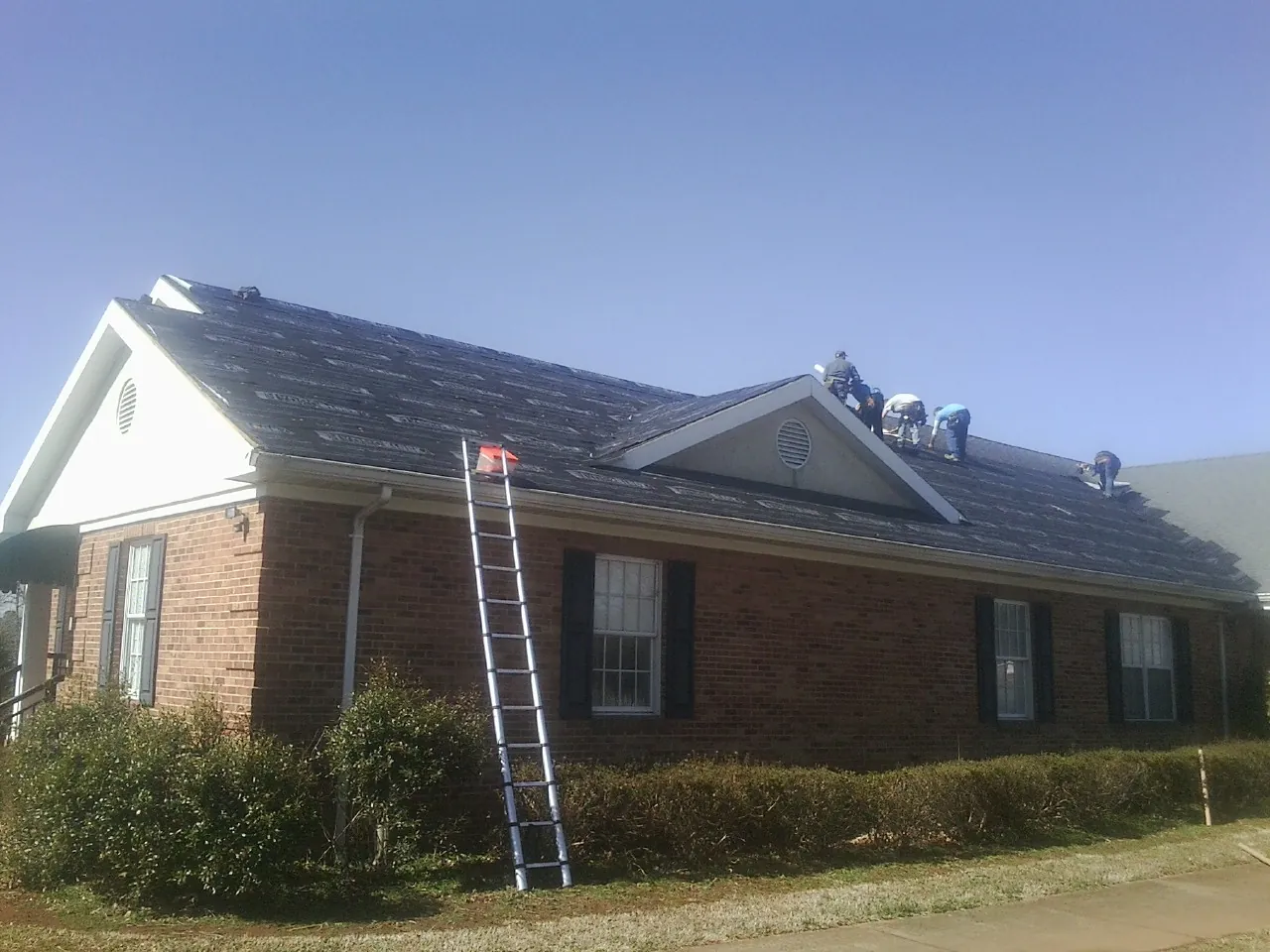 Crew tearing shingles off a brick ranch roof with a ladder set — Metal Roof Repair work by our crew in Ceres
