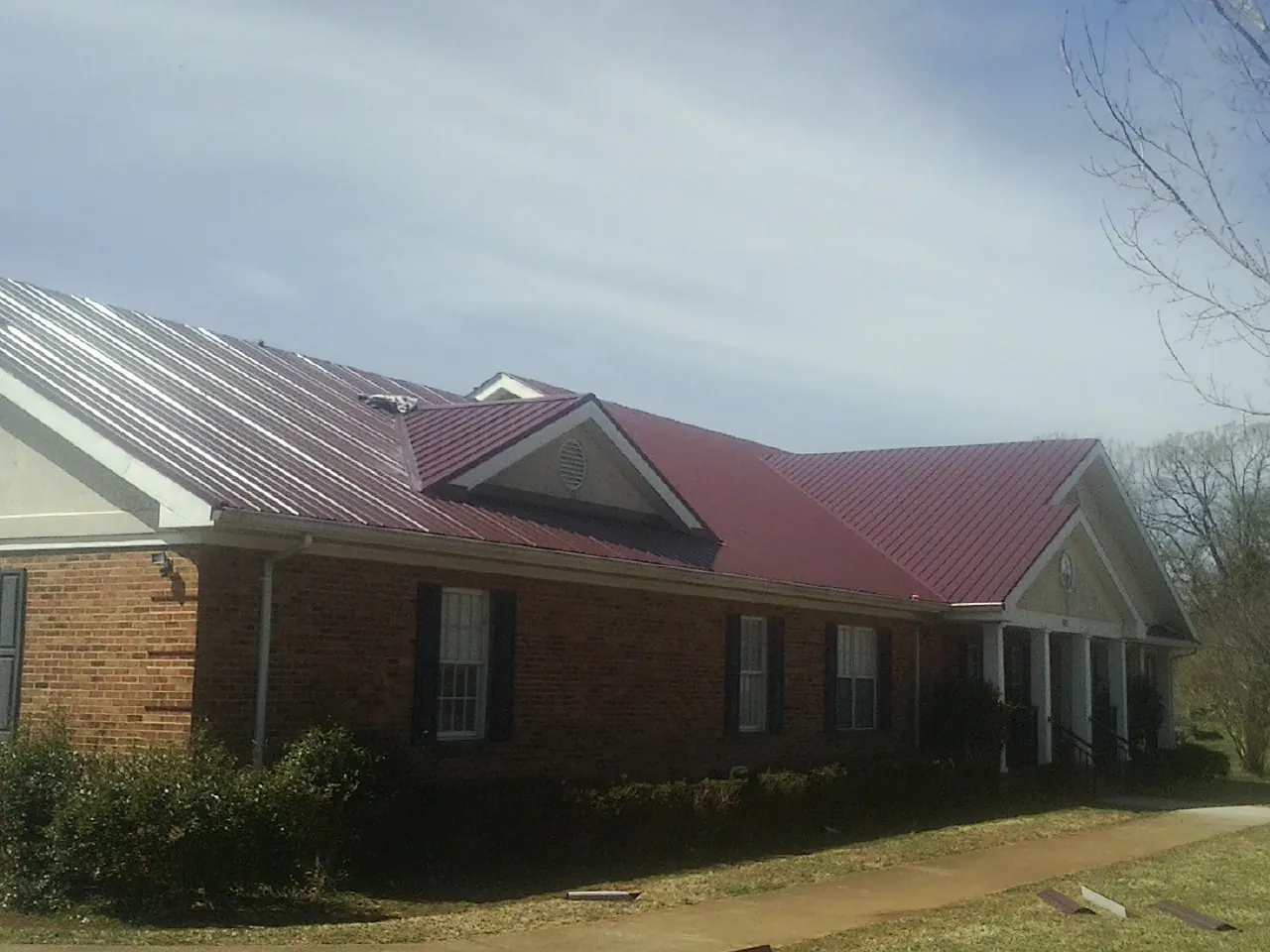 Red metal roof with gabled entries on a long brick building, from a Hail Damage Roof Repair job in Ceres
