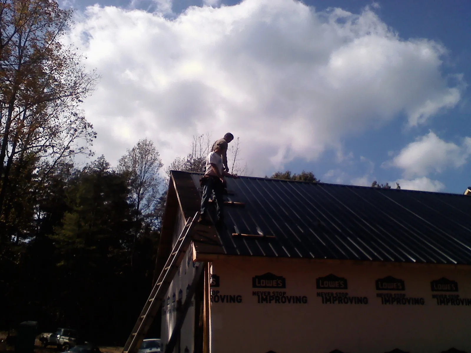 Roofer fastening dark metal panels high against a cloudy sky, from a Roof Inspection job in Ceres